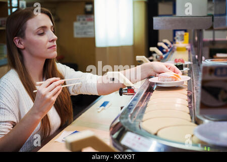 Junge kaukasier Frau sitzt in einer Sushi Bar, ein Gericht aus einem Zug, Kaiten Sushi-zushi. Stockfoto