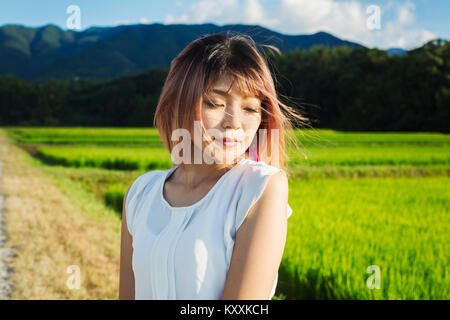 Eine junge Frau in einem weißen Hemd, Haare im Wind, stehen im offenen Raum von Reis Reisfelder. Stockfoto