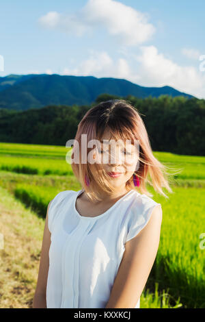 Eine junge Frau in einem weißen Hemd, Haare im Wind, stehen im offenen Raum von Reis Reisfelder. Stockfoto