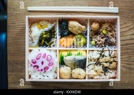 Hohen Winkel in der Nähe von Bento Box mit traditionellen japanischen Speisen und Essstäbchen auf einem Holztisch. Stockfoto