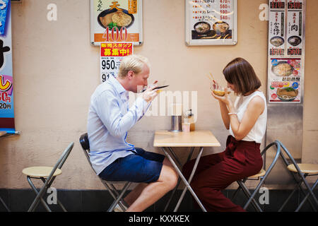 Junger Mann und eine Frau an einem Tisch in einem asiatischen Fast Food Restaurant sitzen, essen von Schalen. Stockfoto