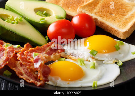 Lecker und herzhaftes Essen: Zwei Spiegeleier mit Speck, Avocado, Toast und Tomate Makro auf einem Teller. Horizontale Hintergrund Stockfoto