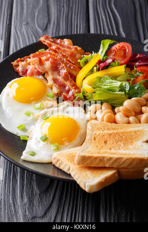 Englisch, hausgemachtes Frühstück: Spiegeleier mit Speck, Bohnen, Toast und frischem Gemüse auf einem Teller auf den Tisch. Vertikale Stockfoto