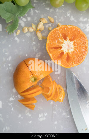 Tangerine auf einem Schneidebrett mit Trauben, Samen und Messer in Scheiben geschnitten werden Stockfoto