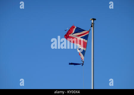 Ein tattered Union Jack Flagge im Wind flattern vor blauem Himmel. Stockfoto