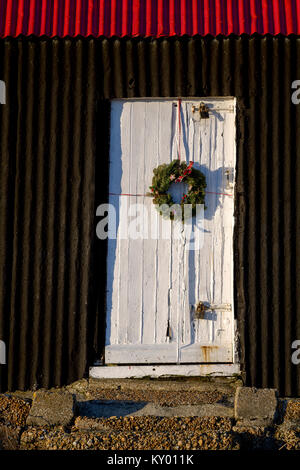 Weihnachten Kranz ist auf der weißen Tür der schwarzen und roten Hütte in Roggen Hafen platziert. Stockfoto