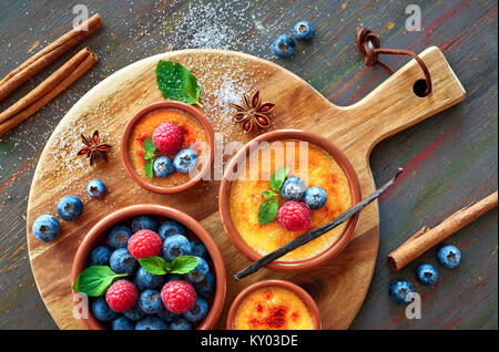 Crème Brûlée (Creme brulee, Gebrannte Creme) Schüsseln mit mit Himbeere, Heidelbeere und Minze auf runde Holzplatte eingerichtet Stockfoto