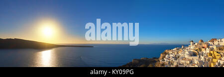 Sonnenuntergang über der Insel Santorini in Griechenland. Traditionelle Kirche, Apartments und Windmühlen im Dorf Oia auf einen Sonnenuntergang, panorama bild. Stockfoto