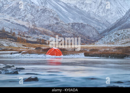 Winter oder Herbst in den Bergen. einsamen Campingplatz und einem Fluss oder einem See. Rote Zelt ist am Ufer des Flusses entfernt. Gelände präsentiert felsigen Hochland zu w Stockfoto