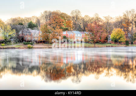 Sonnenaufgang auf Braddock See in Burke, Virginia, USA, Fairfax County mit Reflexion von Stadthäusern, Dunst, Nebel auf der Wasseroberfläche im Herbst und Orangenbäumen Stockfoto