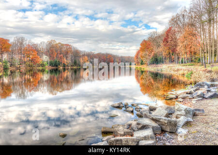 Sonnenuntergang am See Woodglen in Fairfax, Virginia in der Nähe von Wohngebiet, mit orange Laub Herbst Bäume Wald, Wasser Reflexion, Häuser, rocky b Stockfoto