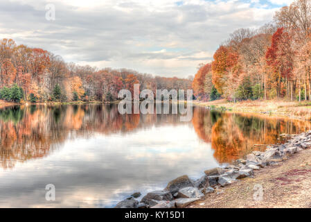 Sonnenuntergang am See Woodglen in Fairfax, Virginia in der Nähe von Wohngebiet, mit orange Laub Herbst Bäume Wald, Wasser Reflexion, Häuser, rocky b Stockfoto