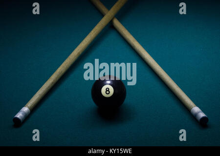 Schwarze Kugel acht auf einem grünen Billard Tisch mit zwei cue Sticks in V-Form Stockfoto