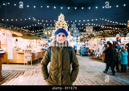 Tallinn, Estland. Junge schöne Hübsche kaukasische Mädchen Frau gekleidet in grüne Jacke und Blaue Hut das Leben genießen Und lächelnd auf Hintergrund Weihnachten X Stockfoto