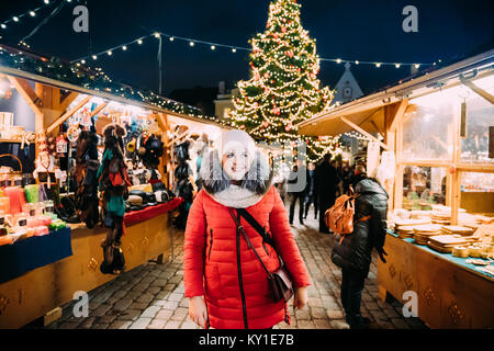 Tallinn, Estland. Junge schöne Hübsche kaukasische Mädchen Frau gekleidet im roten Mantel und dem weißen Hut das Leben genießen Und lächelnd auf Hintergrund Weihnachten Xm Stockfoto