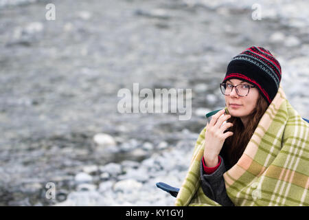 Roter Kopf Frau, die in der camping Stuhl in plaid Decke sitzen. Schön und Gemütlich, entspannend. Stockfoto