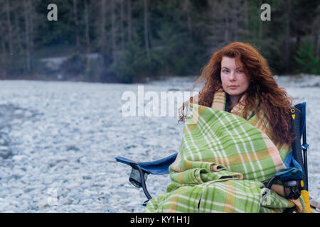 Roter Kopf Frau, die in der camping Stuhl in plaid Decke sitzen. Schön und Gemütlich, entspannend. Stockfoto