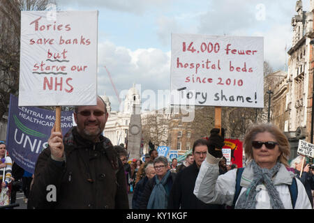 Demonstration für die NHS mit zwei Demonstranten, man/frau lächelnd mit Poster "Tories Banken retten, aber verhungern NHS'' 14k weniger Betten. Tory Schande" Stockfoto