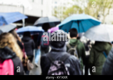 Ein Defokussierten blur Hintergrund von Menschen zu Fuß unter dem Regen durch Sonnenschirme in einer Straße, einer Stadt geschützt Stockfoto