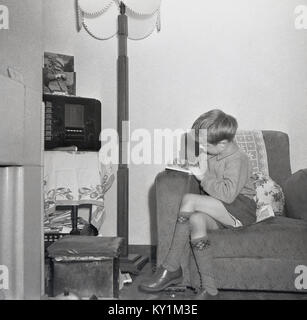 1950, historische, Junge in einem Sessel sitzen in einem Zimmer vorne Schreiben in sein Notebook mit einer WLAN-Radio in der Ecke, England, UK. Stockfoto