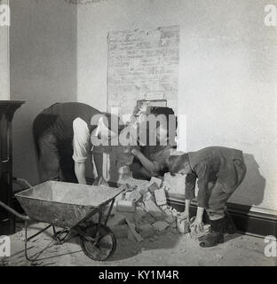 1950, historische, Renovierung, zwei Handwerker oder Bauunternehmer arbeiten an einer Innenwand, Klopfen durch eine Öffnung im Mauerwerk, mit Jugendlichen helfen, die Trümmer zu entfernen, England, UK. Stockfoto