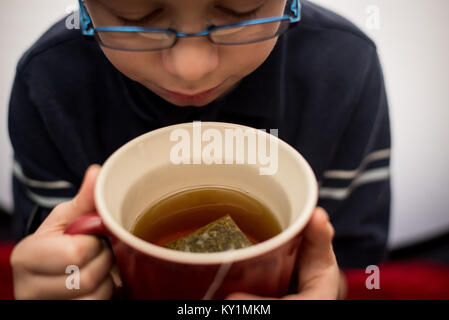 Ein 11-jähriger Junge schaut auf eine Tasse warmen Tee und bereitet sie zu trinken sein kalt während der Grippesaison zu helfen. Stockfoto