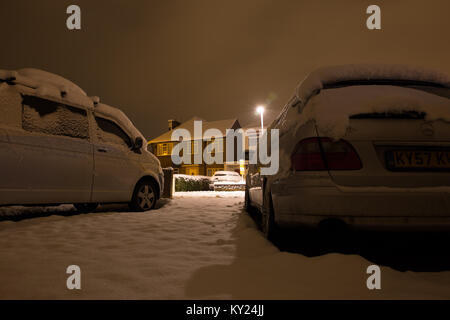 Verschneite Straße Szene auf einem kalten Dezember Abend, von der Einfahrt zu einem der Häuser. Straße Licht erstrahlt. Alle ruhig, alles ist weiß. Stockfoto