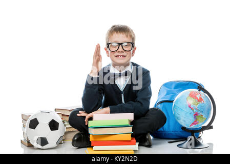 Schüler 8 Jahre alt mit erhobener Hand für die Antwort der Lektion, sitzt auf einem weißen Hintergrund mit Bücher Stockfoto