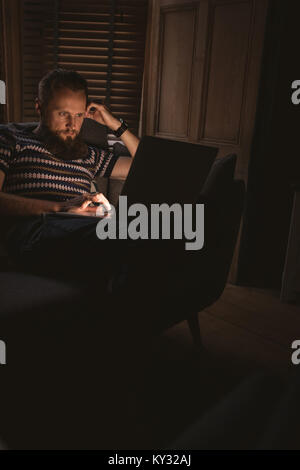 Mann im dunklen Zimmer sitzen auf einem Sofa mit seinem Laptop zu Hause Stockfoto