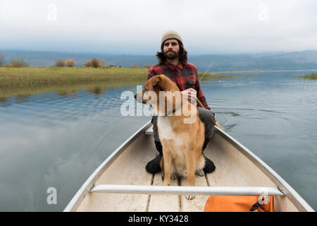 Mann oaring Kanu in Fluss mit seinem Hund an Bord Stockfoto