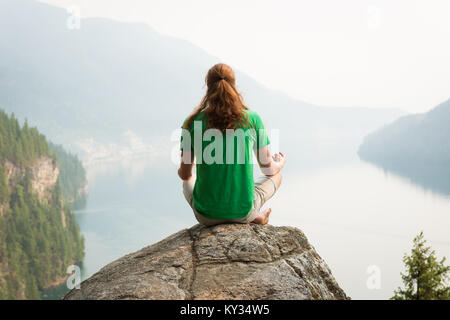 Passen Mann in Meditation Haltung auf dem Rand von einem Felsen sitzend Stockfoto