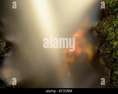 Wehr in Bergbach. Bunte Blätter auf Steinen im kalten, dunklen Wasser. Shinning Blasen erzeugen helle Spuren auf Wasser. Dunkelgrün bemooste Boulder Stockfoto