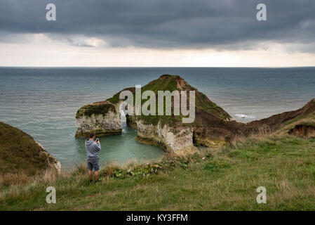 Junger Mann Fotografieren die Landschaft bei hohen Stapeln, Flamborough Head auf seinem Handy. North Yorkshire, England. Stockfoto