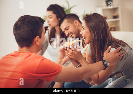 Vier Fröhlichen Freunden heraus hängen in einer Wohnung. Sie haben Spaß und essen Pizza. Selektive konzentrieren. Stockfoto