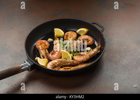 Große Tiger Garnelen Garnelen mit Knoblauch, Zitrone, Gewürze und italienische Petersilie garnieren in einem schwarzen Topf auf einem dunklen Stein Hintergrund Kopf Stockfoto