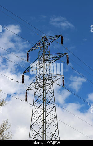 Hohe Spannung Strom pylon oder Energieübertragung Turm mit Kabel. Blauer Himmel mit weißen Wolken im Hintergrund. Einige Zweige sichtbar. Stockfoto