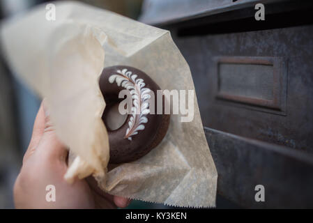 Sehr leckere Schokolade Donut mit Rosetta Holding in Papier wickeln mit Rost Hintergrund Stockfoto