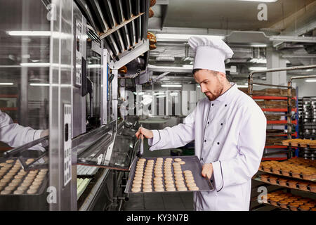 Ein Mann Bäcker mit ein Tablett mit Cupcakes in einer Bäckerei Stockfoto