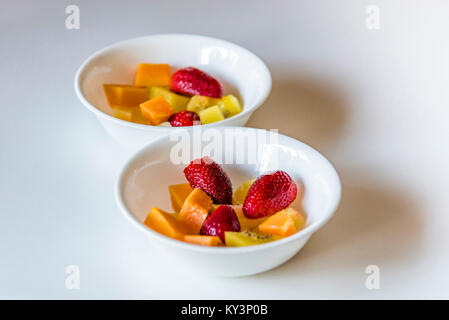 Bunter Salat von frischen Früchten in weißen Schalen, Seitenansicht. Zwei weiße Gerichte der Cut up gesundes Obst, weißer Hintergrund, Nahaufnahme. Stockfoto