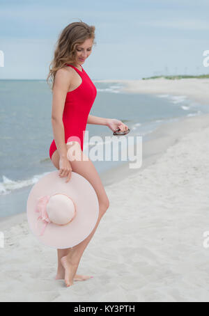 Schöne Frau in einem roten Badeanzug in einen Hut am Strand Stockfoto
