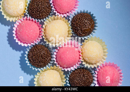 Brasilianische Spezialitäten: Brigadeiro, Beijinho und Bicho de Pe. Kindergeburtstag. Gemeinkosten der Süßigkeit, die Kugel auf blauen Tabelle. Stockfoto