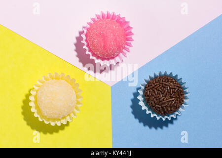 Brasilianische Spezialitäten: Brigadeiro, Beijinho und Bicho de Pe. Kindergeburtstag. Flache Ausführung von candy Kugel auf farbigen Hintergrund. Stockfoto