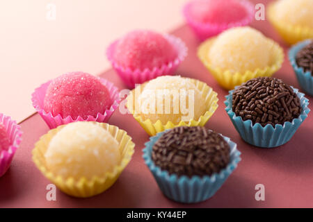 Brasilianische Spezialitäten: Brigadeiro, Beijinho und Bicho de Pe. Kindergeburtstag. Candy Kugeln in einer geraden Linie. Bunter Hintergrund. Stockfoto