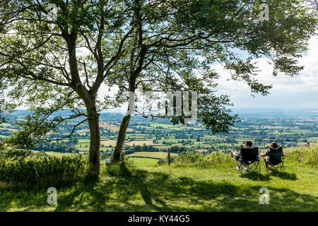 Junges Paar sitzt auf dem Falten Campingstühle und genießen Sie den herrlichen Panoramablick von Coaley Peak Picknickplatz und Aussichtspunkt, Dursely, Gloucestershire, VEREINIGTES KÖNIGREICH Stockfoto