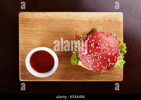 Red Burger mit Schnitzel, Speck und Gemüse, bestreut mit Sesam auf einer Tafel Stockfoto