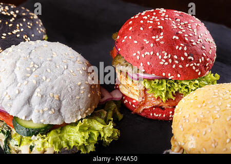 Eine Menge Hamburger auf andere Farbe Brötchen, mit Gemüse, Käse, Koteletts und Fleisch ist auf einem Holzbrett. Sortiment von Fast Food Stockfoto