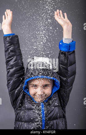 Happy little boy im Winter Kleidung mit den Armen über grauer Hintergrund angehoben Stockfoto