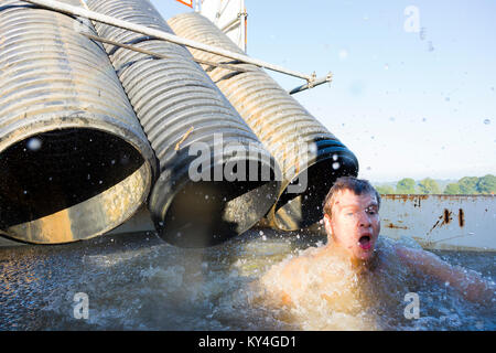 Sussex, UK. Ein junger Mann zieht eine entsetzte Gesicht, als er aus einem Pool von einfrierendem Wasser während einer haltbaren Mudder Hindernisparcours entsteht. Stockfoto