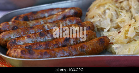 Close up Teil der gegrillten Nürnberger Bratwurst Bratwurst mit Beilage von Sauerkraut auf Metall Zinnteller, Low Angle View Stockfoto