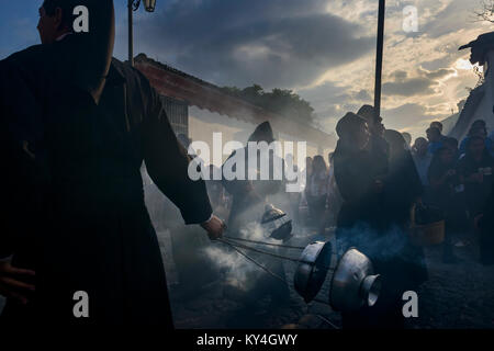 Antigua, Guatemala - 19. April 2014: Silhouette der Männer in schwarzen Roben und Hauben Räucherwerk verbreiten sich in einer Strasse der Stadt Antigua während einer pro Stockfoto